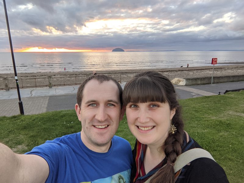 Dean and Miriam on a beach at sunset, with the sea and a distant island behind them
