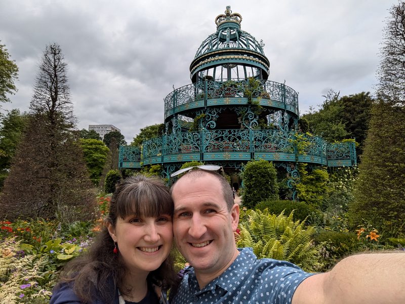 Dean and Miriam in a garden, in front of an ornate ironwork bandstand